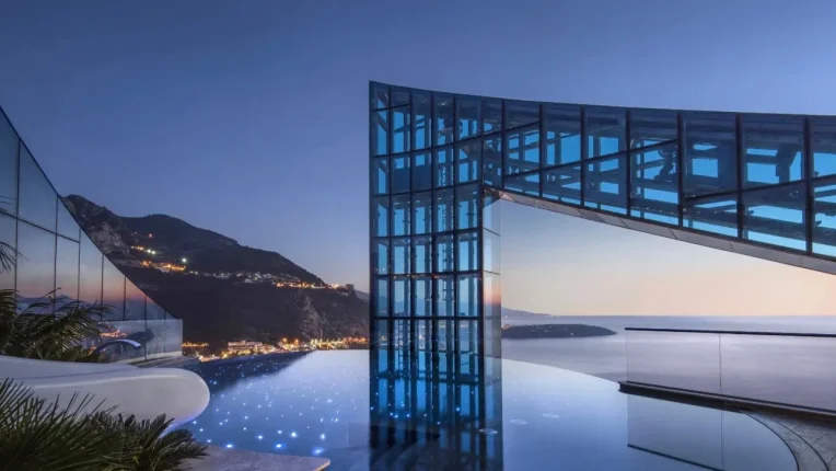 The pool of the Penthouse of Tour Odéon residence in Monaco. In this photo you see the pool and design elements of the building. In the background you see mountains, roquebrune-Cap-Martin, and the ocean