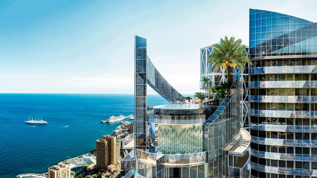 This photo shows the penthouse of the Tour Odeon Residence, located in Monaco. You see the top floor of the building with palm tree and pool on top. Additionally you see other residences, such as Roccabella, and the Mediterranean sea.