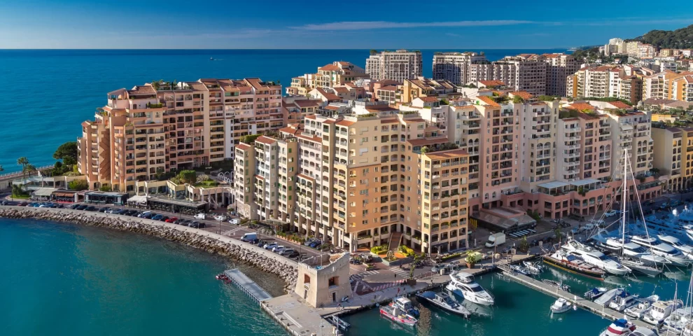 A view of the eden star residence with the rest of the fontvieille district in the background. You see the building port, restaurants, streets and cars.