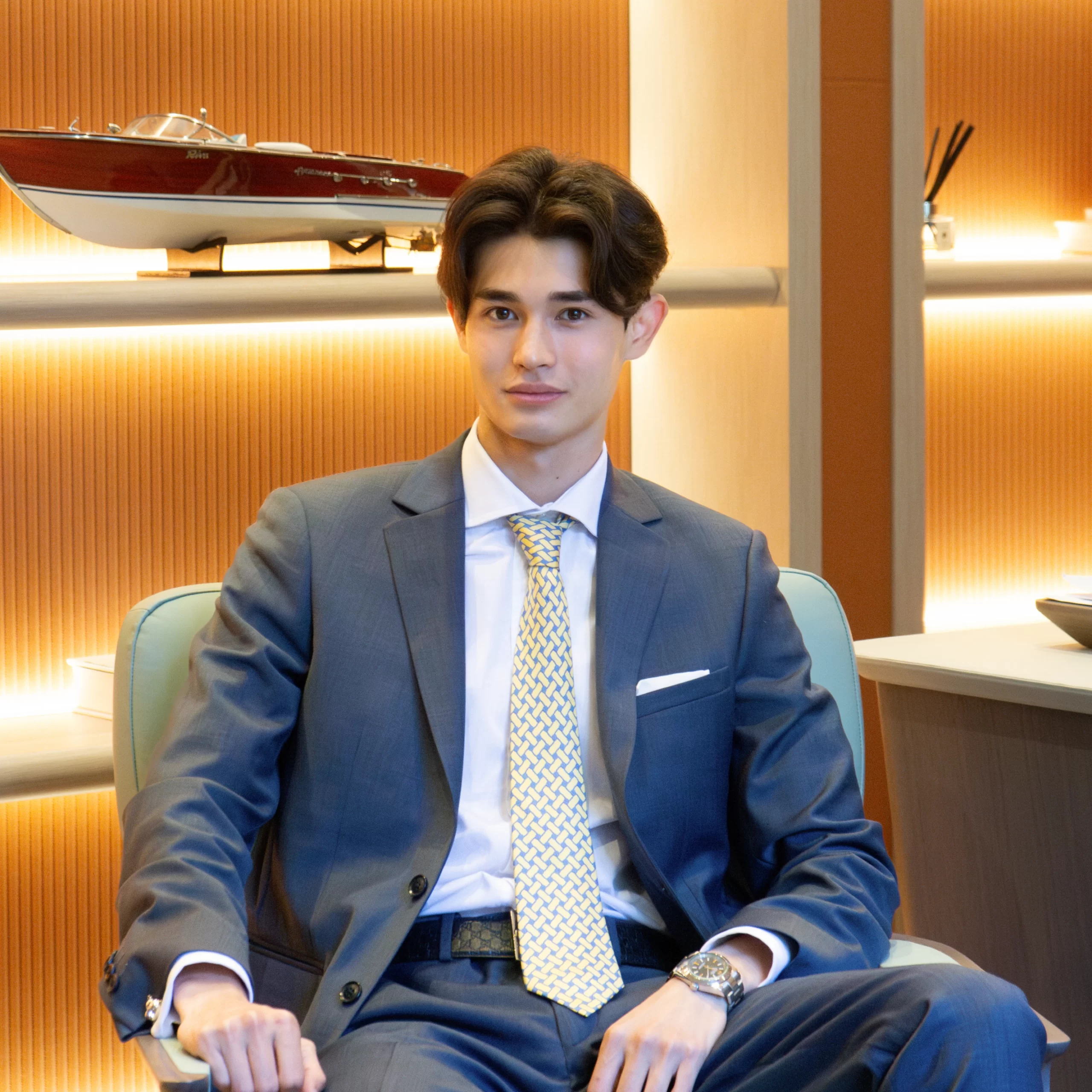 A photo of Richard Lee Canali. You see Richard in a suit with an Hermes Tie and Rolex. In the Background you see a shelf with a model Riva Yacht.