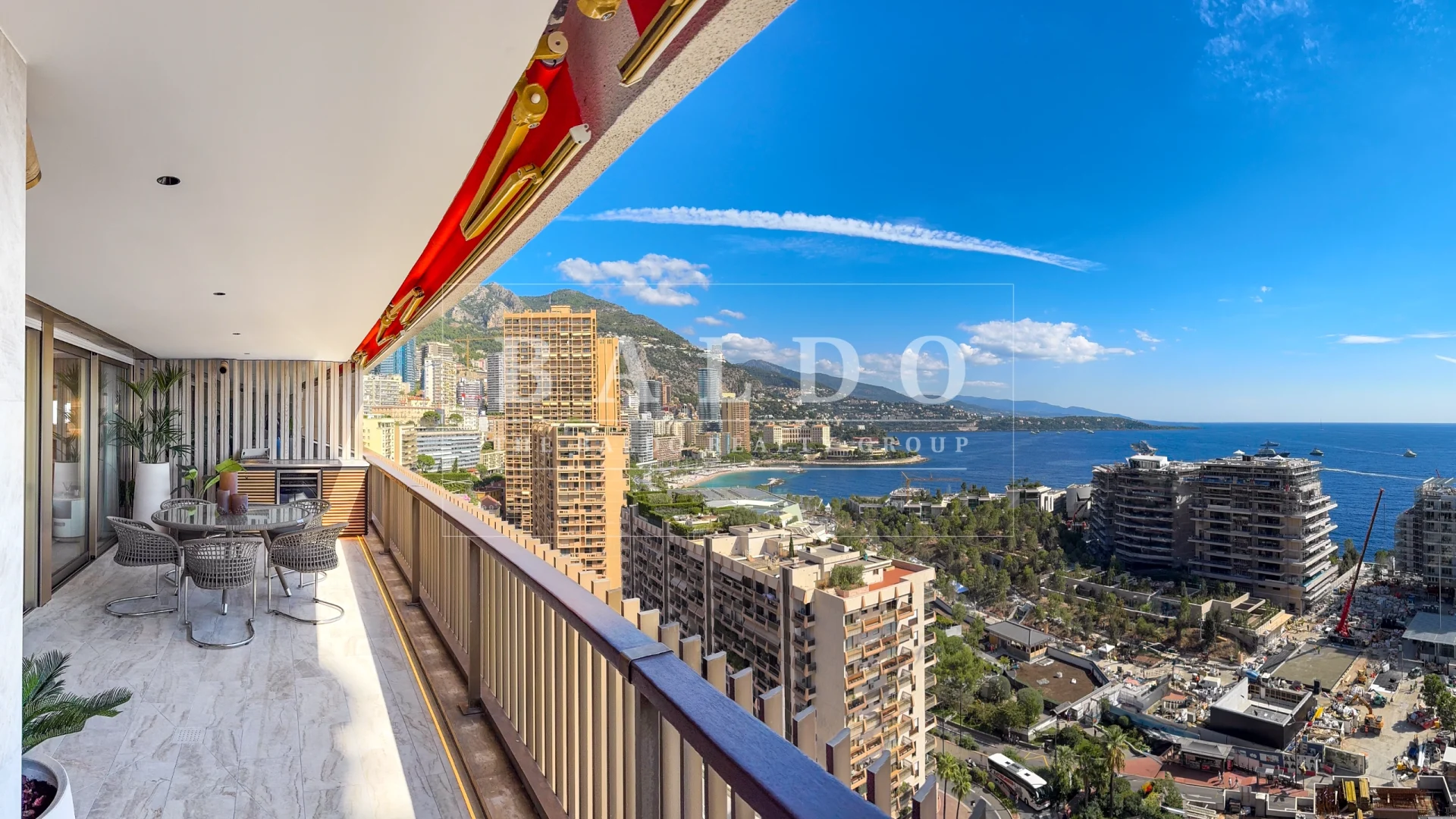 A picture of the balcony and view of an apartment in Le Mirabeau. You see the terrace, outdoor kitchen, table, and view of Larvotto Beach, Grimaldi Forum