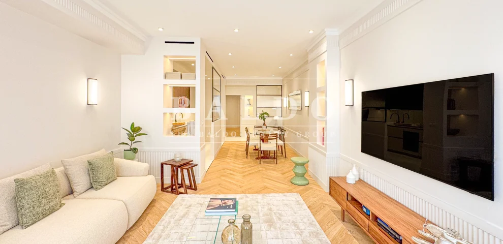 The living room of a renovated apartment in the Le Victoria residence in Monaco. In this photo you see a living room with a couch, coffee table, and tv. In the background you see the dining room of the apartment