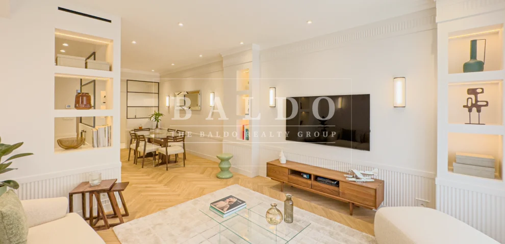 The living room of a renovated apartment in the Le Victoria residence in Monaco. In this photo you see a living room with a couch, coffee table, and tv. In the background you see the dining room of the apartment