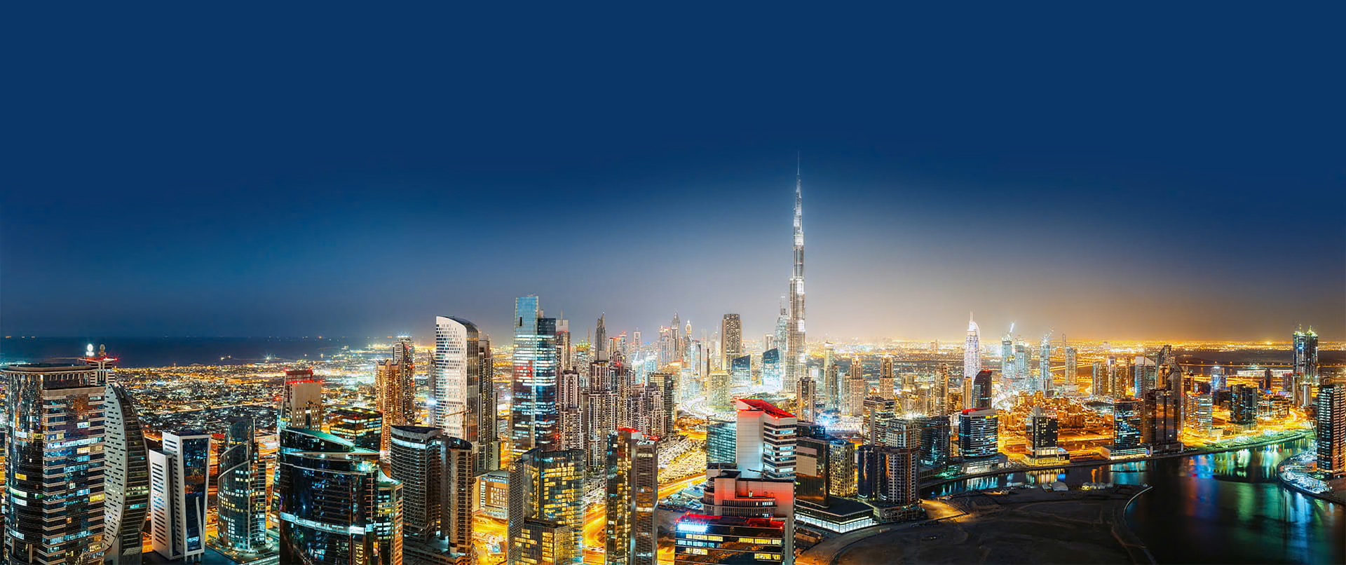 In this photo you see a night skyline of Dubai featuring the Burj Khalifa. In the background.