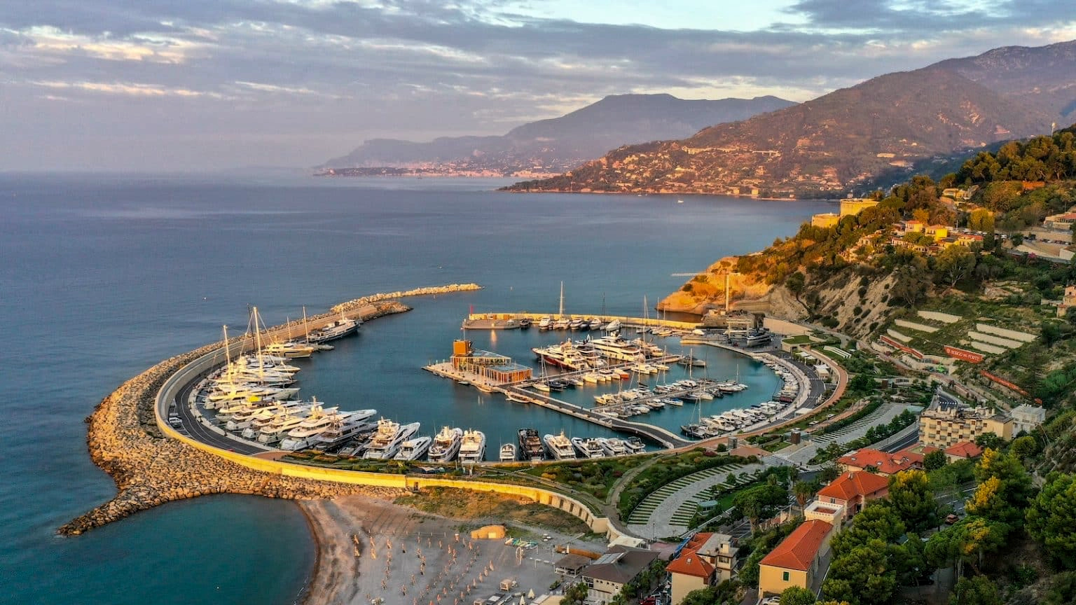 An aerial photo of the Cala del Forte port in Ventimiglia Italy. In this photo you see the round port with yachts, and in the background you see the French Riviera and Monaco