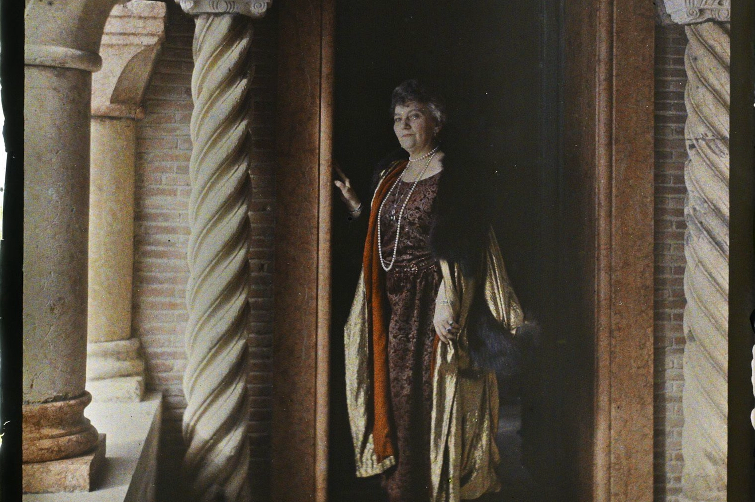 Cyprienne Douine in pearls and a gold cloak, standing in a doorway between spiral marble columns at Villa Cypris, 1923 autochrome